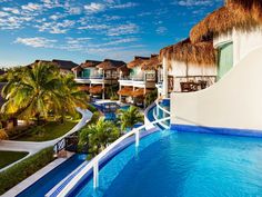 an outdoor swimming pool surrounded by palm trees and thatched roof huts with water slides