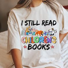 a woman sitting on top of a bed wearing a t - shirt that says i still read children's books