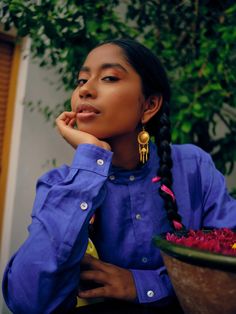 a woman sitting in front of a potted plant with her chin resting on her hand