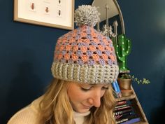 a woman wearing a crocheted hat looking at her cell phone in front of a mirror