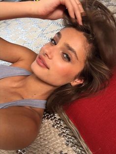 a beautiful woman laying on top of a bed next to a red pillow with her hand on her head