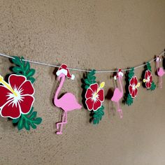 some pink flamingos and red flowers are hanging from a line on the wall,