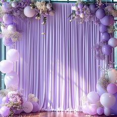 a purple and white backdrop with balloons, flowers and greenery on the floor in front of it