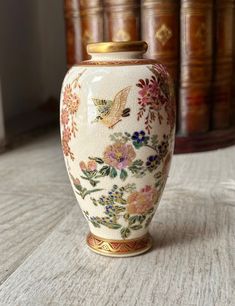 a white vase with colorful flowers on it sitting on a table next to some books