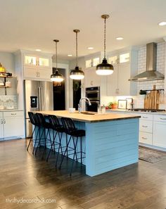 a large kitchen with an island in the middle and three lights hanging from the ceiling