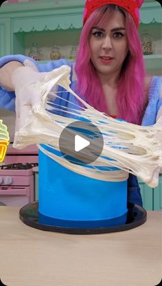 a woman with pink hair is making something out of a blue bucket on a table