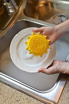 a person holding a white plate with a yellow flower on it in front of a sink