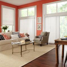 a living room with orange walls and white blinds on the window sill, coffee table in between two chairs