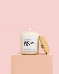 a white candle sitting on top of a pink block next to a jar of deodorant era