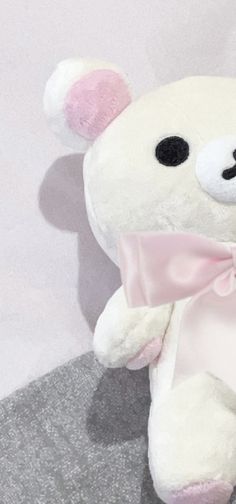 a white teddy bear with a pink bow on it's neck sitting on a gray surface