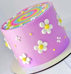 a pink cake decorated with white flowers and rainbow swirls