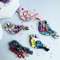 four colorful bird brooches sitting on top of a white table with confetti scattered around them