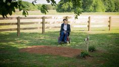 a man sitting in a wheel chair on top of a lush green field next to a wooden fence