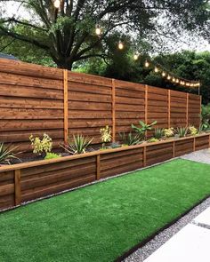 an outdoor garden with artificial grass and wooden fenced in areas that have lights strung from the trees