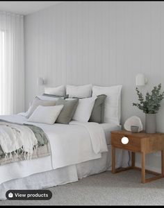 a bed with white sheets and pillows next to a small wooden table in front of a window