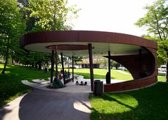 people are sitting on benches in the shade under an awning at a public park