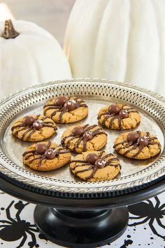 cookies with chocolate drizzled on them sitting on a metal platter next to white pumpkins