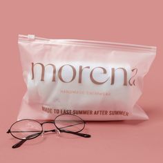 a pair of glasses sitting on top of a pink surface next to a bag of sunscreen