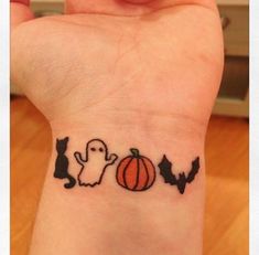 a person with a small tattoo on their wrist that has a ghost, cat and pumpkin