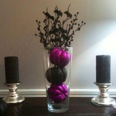 a vase filled with purple and black balls on top of a table next to two candles