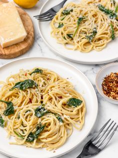 two plates of pasta with spinach and parmesan cheese next to some bread