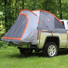 a truck with a tent attached to it's bed parked in the grass near trees