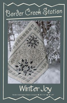 a white and black quilted blanket sitting on top of snow covered ground next to trees