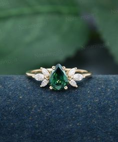 an emerald and white diamond ring on top of a blue cloth with green leaves in the background