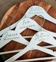 six bridesmaid hangers with names on them sitting on a wooden board in front of a table