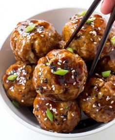 someone is holding chopsticks over some meatballs with sesame seeds in a white bowl