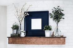 a mantle with potted plants and a mirror on top of it in front of a white brick wall