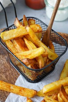 french fries in a basket with a wooden spoon and salt on the table next to them