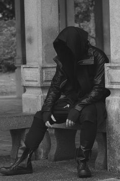 a person sitting on a bench wearing a hoodie and black boots with their hands in their pockets