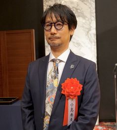 a man in a suit and tie with an orange flower on his lapel pin