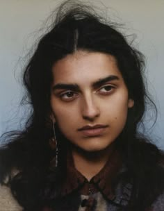 a young man with long hair wearing a sweater and earrings, looking at the camera