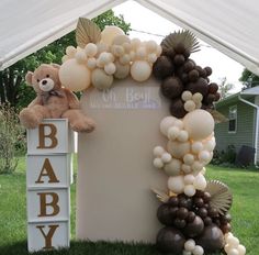 a teddy bear sitting on top of a sign with balloons attached to it's sides