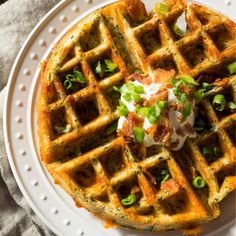 a waffle topped with bacon, green onions and sour cream on a white plate