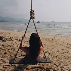 a woman is sitting on a swing at the beach and looking out into the water