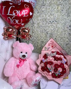 a pink teddy bear sitting next to two heart shaped balloons and a valentine's day bouquet