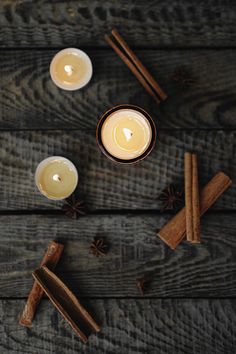 three candles with cinnamon sticks and star anise on a wooden table next to them