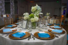 the table is set with blue napkins and gold plates, silverware, and flowers