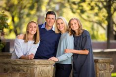 three women and one man are posing for a family photo in front of some trees