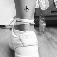 a small tattoo on the ankle of a woman with an airplane in the sky behind her