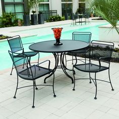 an outdoor table with four chairs and a vase on it next to a swimming pool