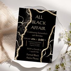 a black and gold birthday party card on a white plate with flowers in the background