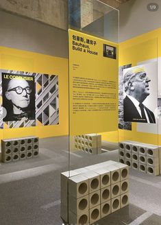 an exhibit with yellow walls and posters on the wall, in front of it is a bench made out of cinder blocks