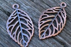 two metal leaf charms sitting on top of a wooden table