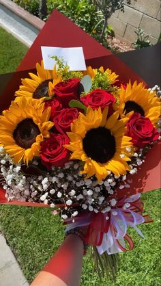 a bouquet of sunflowers and roses in a red paper box on the grass