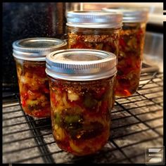 four jars filled with pickles sitting on top of a rack