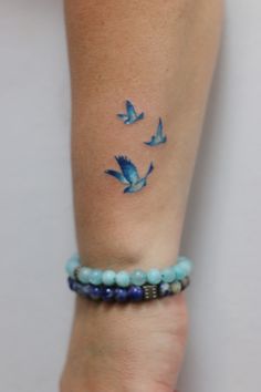 a woman's arm with blue birds on it and beads around her bracelets